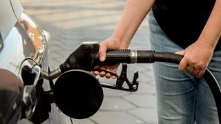 Eine Person hat beim Tanken einen Zapfhahn in der Hand und betankt ein Auto