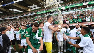 Werder-Spieler feiern ausgelassen mit Bierdusche vor der Ersatzbank nach dem Aufstieg.