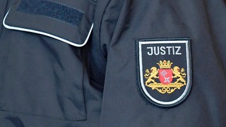 Ein Justizbeamter mit Bremer Abzeichen steht im Gerichtssaal. 