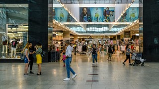 Menschen gehen in einem Einkaufszentrum vor einem Geschäft entlang.