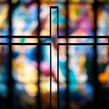 Ein Kreuz zeichnet sich vor einem bunten Glasfenster ab 