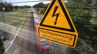 Ein Schild über einer Bahnstrecke warnt vor Hochspannung.