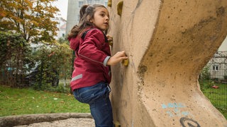 Ein Mädchen klettert auf einem Spielplatz. 