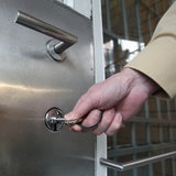 Eine Hand schließt mit einem Schlüssel die Tür einer Gefängsniszelle auf