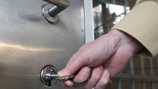 Eine Hand schließt mit einem Schlüssel die Tür einer Gefängsniszelle auf