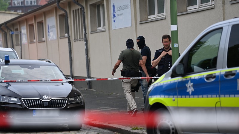 zwei maskierte und ein unmaskierter Zivilpolizist stehen an einem Gebäude