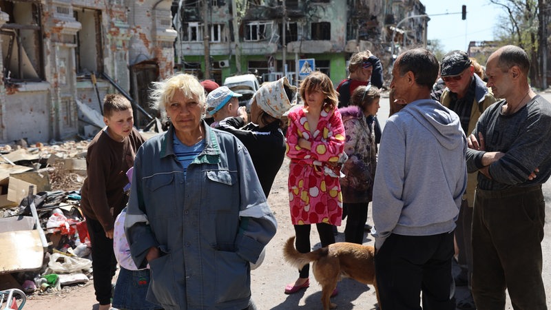 Menschen aus Mariupol stehen vor einem zerstörten Gebäude, 9. Mai 2022