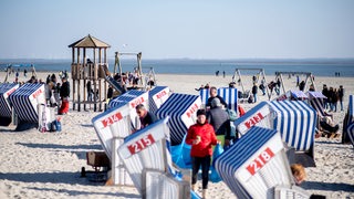 Menschen und Strandkörbe am Strand von Norderney.
