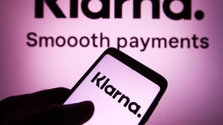 Eine Hand hält ein Smartphone, auf dem das Wort "Klarna" steht