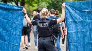 Eine Polizistin hält zwei Sichtschutz-Laken in die Höhe.