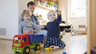 Vater mit zwei Kindern im Alter von neun Monaten und drei Jahren in einer Wohnung beim Spielen