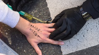 Umweltaktivisten der Gruppe «Letzte Generation» haben sich auf der Fahrbahn fest geklebt und ein Polizist versucht den Kleber zu lösen.