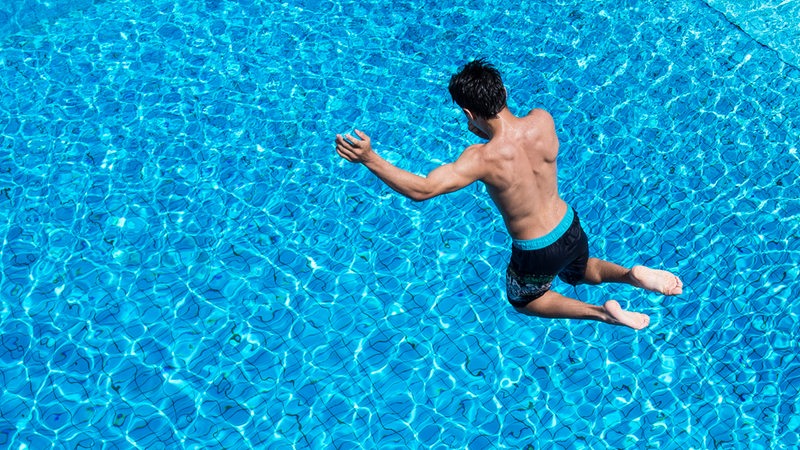 Ein Junge springt in einem Freibad von einem Sprungturm ins Wasser. (Symbolbild)