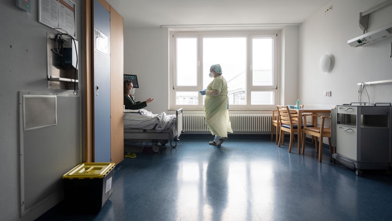 Eine Krankenschwester unterhält sich mit einer Patientin auf einer Normalstation unter Coronabedingungen.