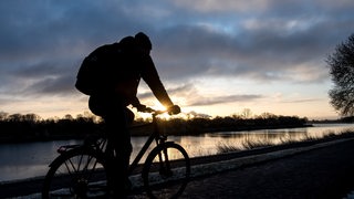Ein Radfahrer fährt bei Sonnenaufgang am Werdersee entlang