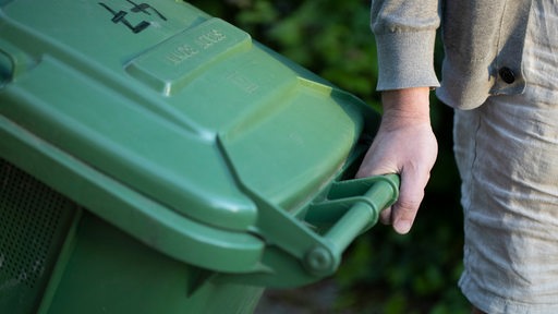 Eine Person zieht eine grüne Mülltonne.