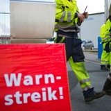 An einem Warnstreikschild gehen Hafenarbeiter vorbei