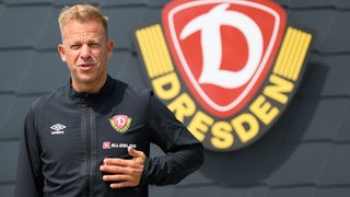 Ex-Werder-Trainer Markus Anfang bei seiner offiziellen Vorstellung als Coach von Dynamo Dresden lächelnd vor dem Vereinslogo.