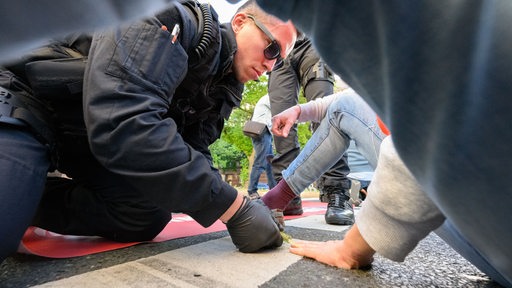 Ein Polizist löst eine festgeklebte Hand von einer Straße