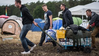Junge Männer ziehen auf einem Festivalgelände einen Bollerwagen mit Getränken