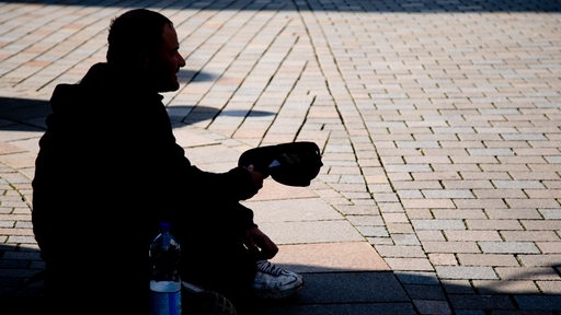 Ein Obdachloser sitzt im Sommer in einer Fußgängerzone und hält den Hut auf.