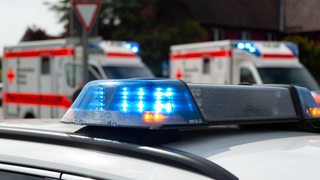 Das Blaulicht eines Polizeiautos blinkt. Im Hintergrund stehen zwei Krankenwagen.