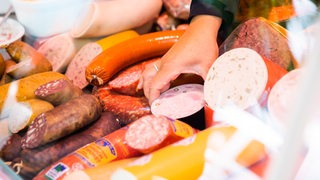 Eine Verkäuferin nimmt auf einem Wochenmarkt im Berliner Ortsteil Schöneberg Fleischwaren aus einer Theke.