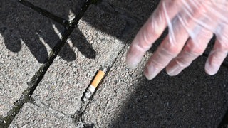 Ein Mann hebt einen weggeworfene Zigaretten-Stummel vom Boden auf.