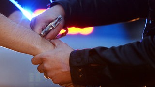 Ein Polizist legt einem Mann Handschellen an.