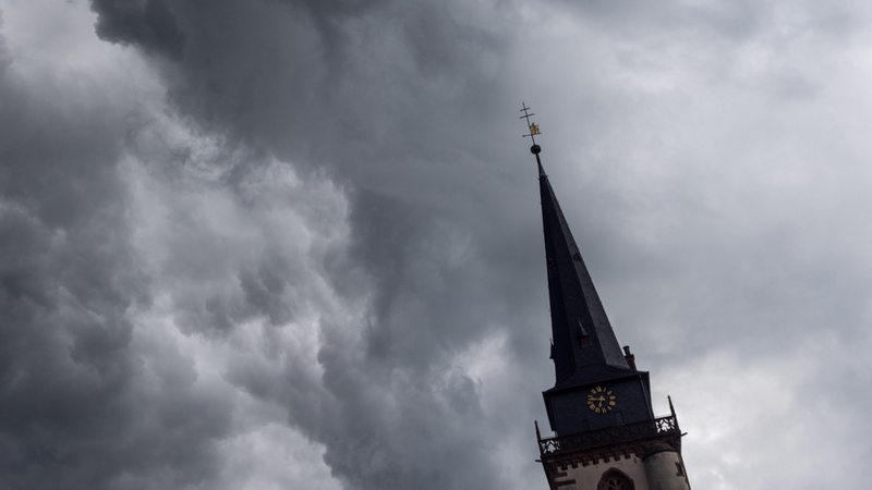Dunkle Wolken sind über einem Kirchturm zu sehen.