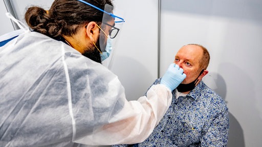 Der Mitarbeiter eines Testzentrums macht einen Nasenabstrich bei einem Mann.