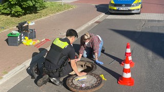 Polizisten untersuchen einen Gully.