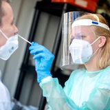 Eine Frau mit Gesichtsmaske und Mundschutz macht einen NAsenabstrich bei einem Mann