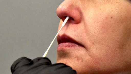 Eine Hand schiebt ein Teststäbchen in die Nase einer Frau
