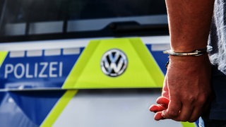 Zwei Hände in Handschellen vor einem Polizeiwagen