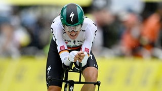 Ein Radprofi mit Helm und Brille beugt sich über das Lenkrad eines Rennrades.