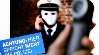 Ein Telefonhörer ist vor einem Plakat der Polizei mit der Aufschrift "Achtung: Hier spricht nicht die Polizei" zu sehen. Das Plakat der Polizei warnt vor Betrügern, die sich am Telefon als Polizisten ausgeben.