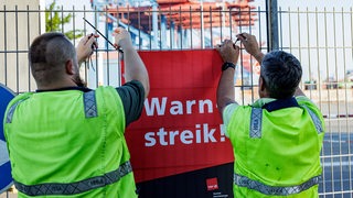 Hafenarbeiter hängen ein Schild mit der Aufschrift "Warnstreik" auf.