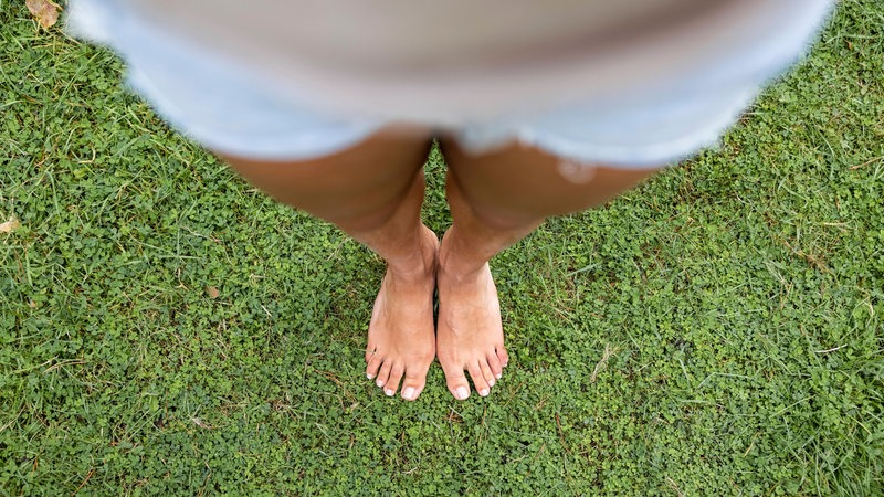 Eine Frau steht auf Gras. Die Kamera fotografiert an ihr herunter.