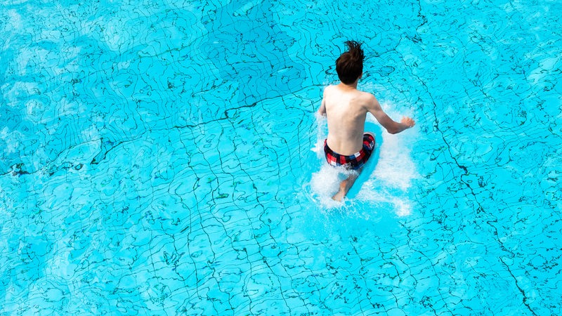 Ein Junge springt in ein Schwimmbecken voll mit blauem Wasser.