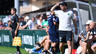 Werder-Trainer Ole Werner steht am Spielfeldrand und fasst sich an die Mütze