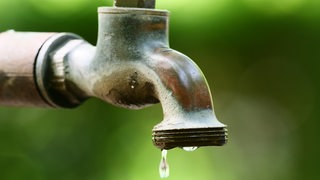 Ein Wassertropfen tropft von einem alten Wasserhahn im Außenbereich.