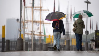 Spaziergänger mit Regenschirmen laufen an der Weserpromenade entlang.