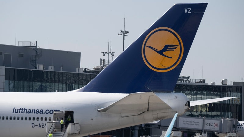 Das Heck eines Lufthansa-Fliegers steht an einem Flughafen.