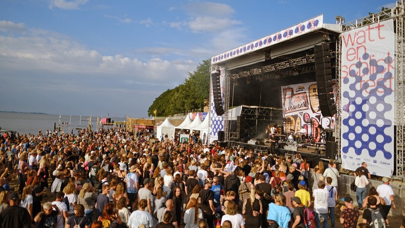 Auf dem Watt En Schlick-Festival am Kurhausstrand in Dangast stehen zahlreiche Menschen vor einer Bühne.
