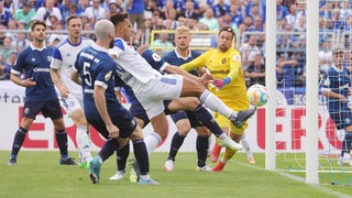 Schalke-Spieler Rodrigo Zalazar spitzelt den Ball trotz der Abwehrversuche der Spieler des Bremer SV zum 1:0 für Schalke ins Tor.