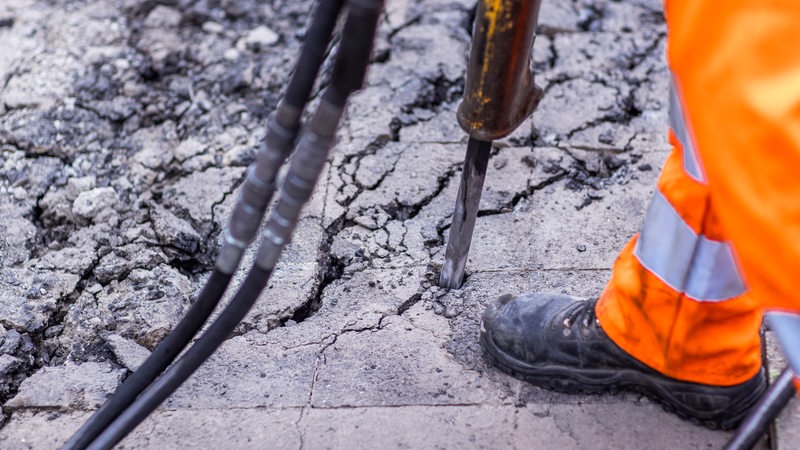 Asphalt wird mit einem Presslufthammer aufgebrochen.