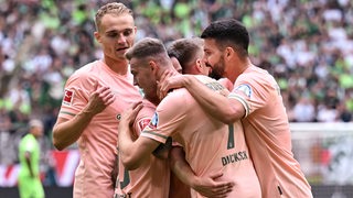 Werder-Spieler in lachsfarbenen Trikots umarmen sich beim Jubel über das Tor gegen Wolfsburg.