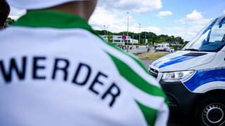Ein Werder-Fan steht vor einem Polizeiwagen.