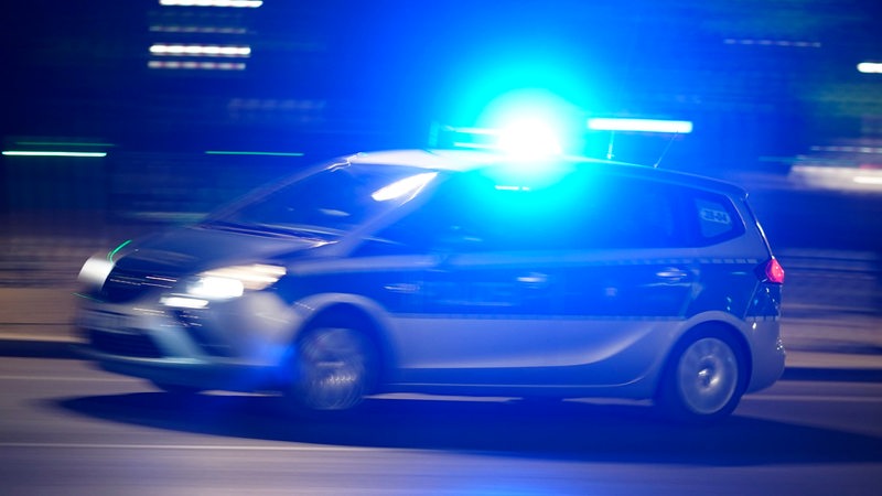 Ein Polizeiauto mit Blaulicht fährt auf einer Straße.